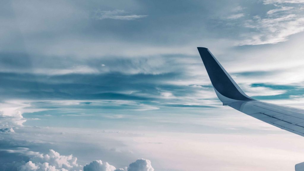 Wingtip of an airplane visible in a clear blue sky with wispy clouds below and to the side.