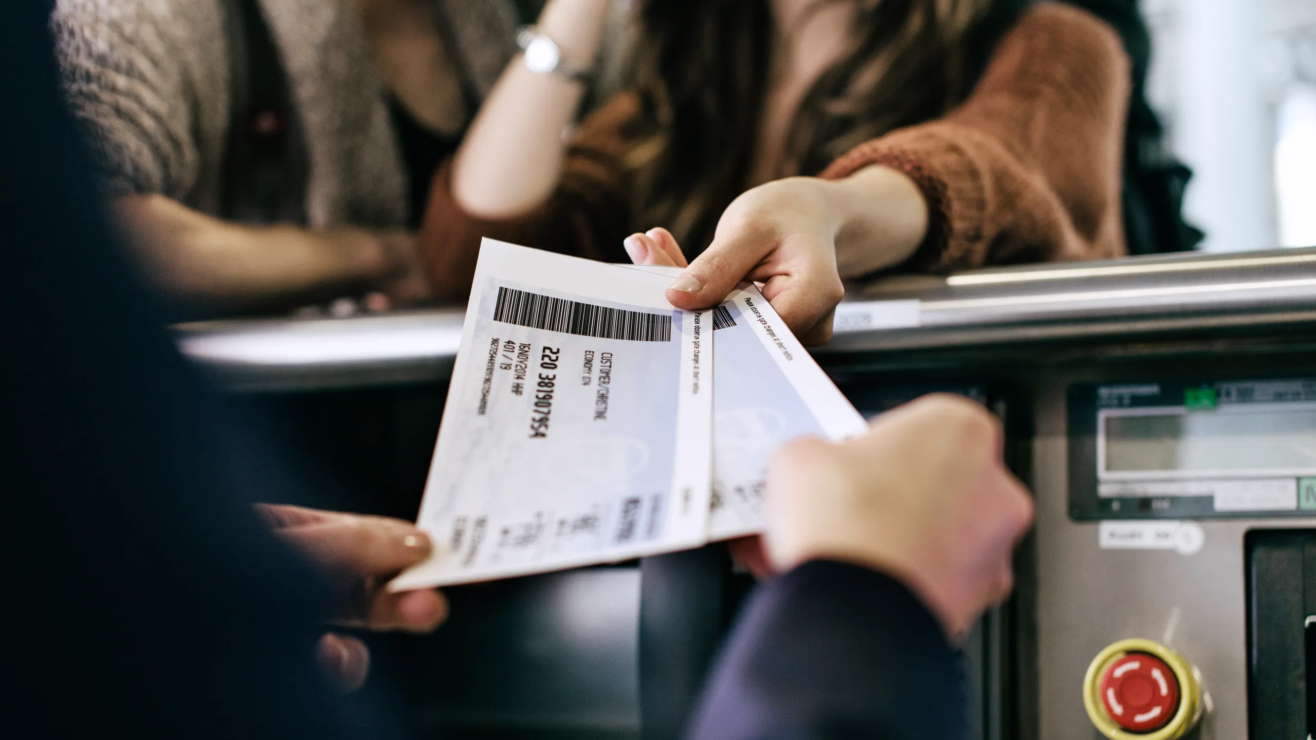 Close-up of hands exchanging printed tickets with barcodes at a checkout scanner.